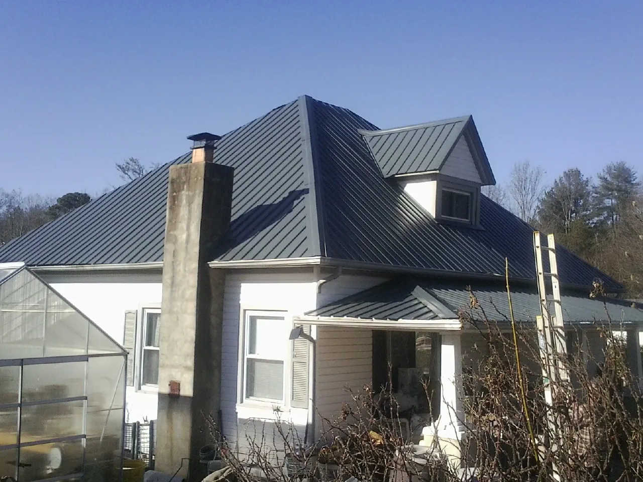 Dark blue standing seam metal roof on a white farmhouse with dormer — Slate & Tile Roof Repair by Roofing Brothers in Larchwood