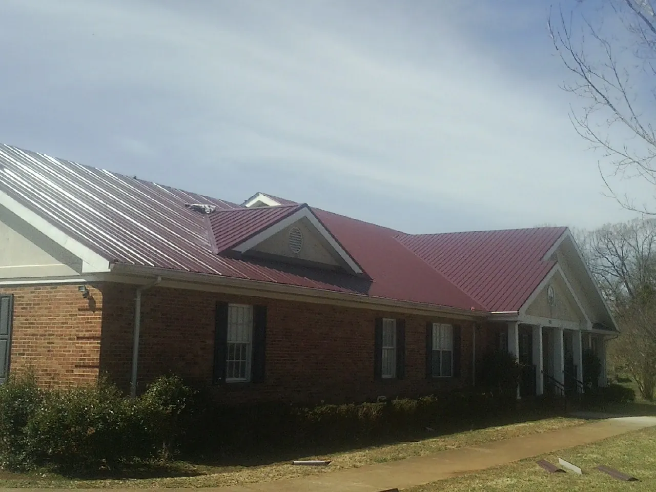 Red metal roof with gabled entries on a long brick building, from a Hail Damage Roof Repair job in Larchwood
