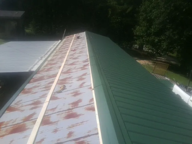 Old rusted panels beside newly installed green metal roofing — Wind Damage Roof Repair by Roofing Brothers in Larchwood