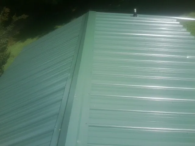 New green metal panels meeting at the ridge of a roof — Flat Roof Repair work by our crew in Larchwood