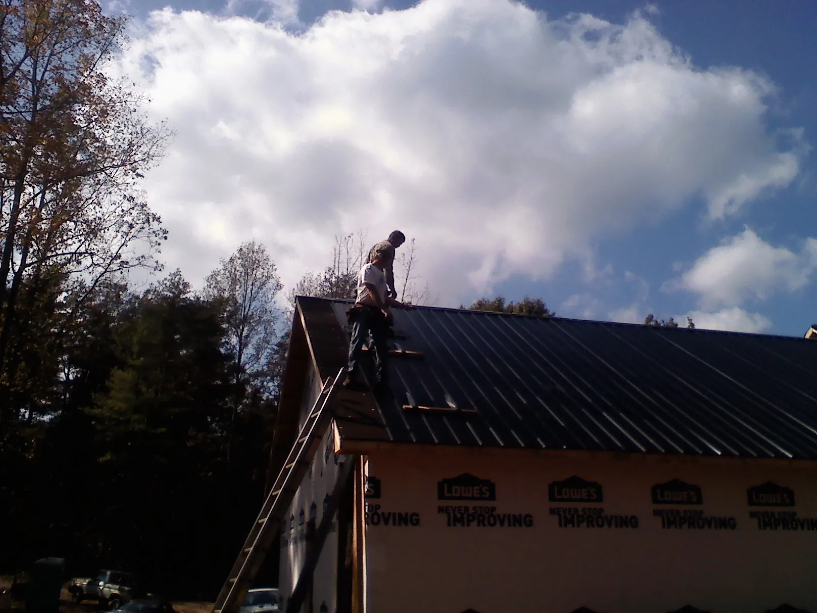 Roofer fastening dark metal panels high against a cloudy sky, from a Roof Inspection job in Larchwood