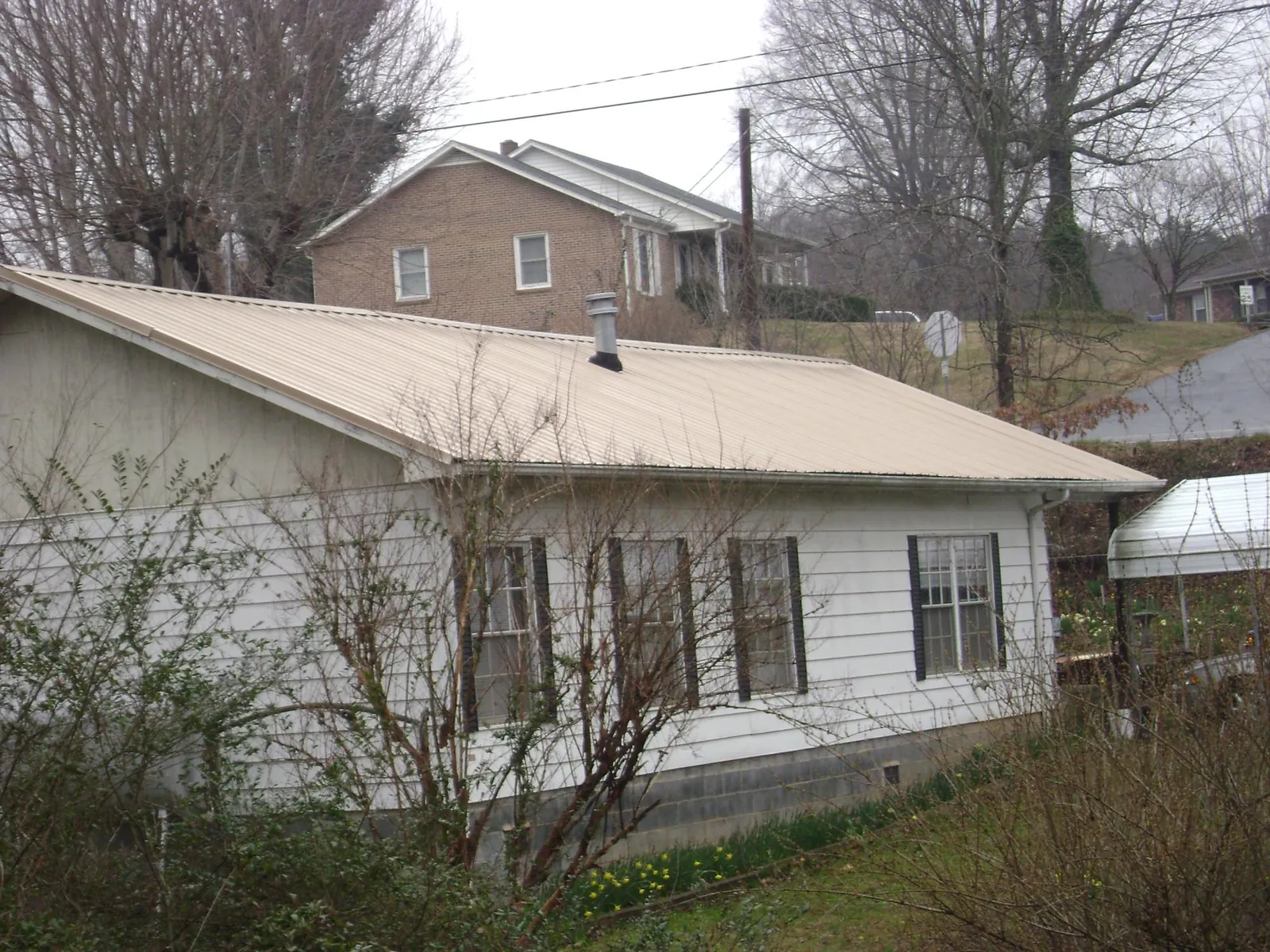 Tan metal roof on a white sided house set into a hillside — Commercial Roofing by Roofing Brothers in Larchwood