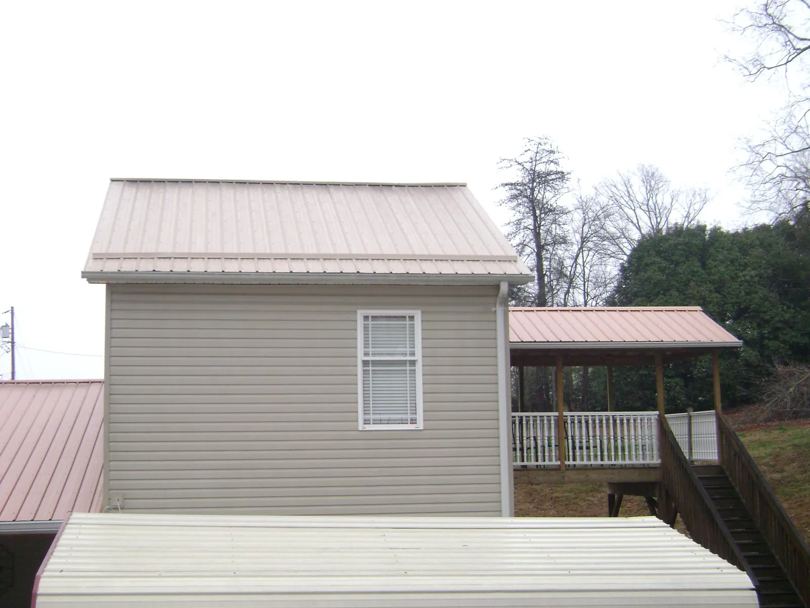 Tan metal roofs on a two story addition and attached porch, from a Roof Replacement job in Larchwood